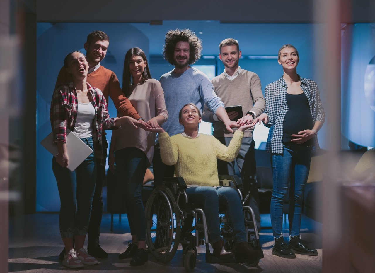 Disabled businesswoman in a wheelchair at the office with coworkers. Portrait of a diverse business team in a modern open space coworking office space. High quality photo
